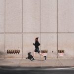 A person jogging along a city sidewalk against a modern urban wall, embracing an active lifestyle.